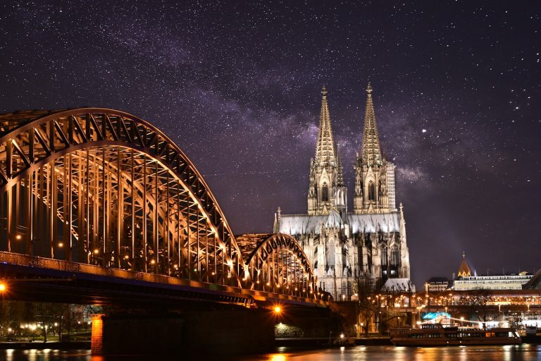 Kölner Dom und Hohenzollernbrücke bei Nacht mit sternenklarem Himmel.