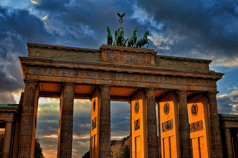 Das Brandenburger Tor vor dramatischem Himmel, beleuchtet bei Sonnenuntergang.